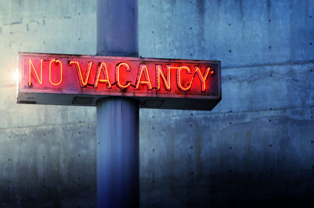 shutterstock_151308128 Glowing retro neon 'no vacancy' sign against cool blue wall background