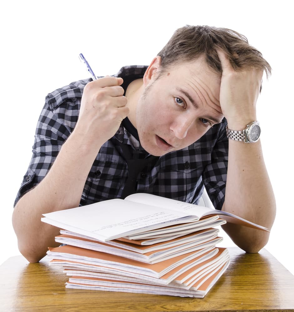 shutterstock_162205595 Tired, stressed male teacher marking books. Isolated image on white background. 