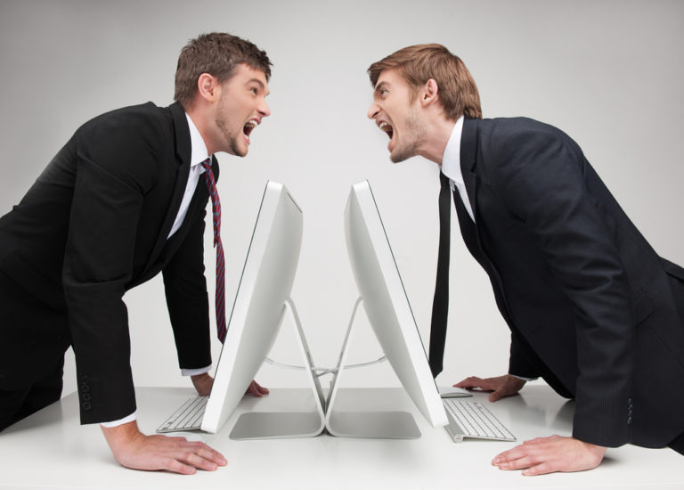 shutterstock_149698517 MenÃ?Â¯Ã?Â¿Ã?Â½ confrontation. Two angry young business people standing face to face and holding their hands at the table while isolated on grey