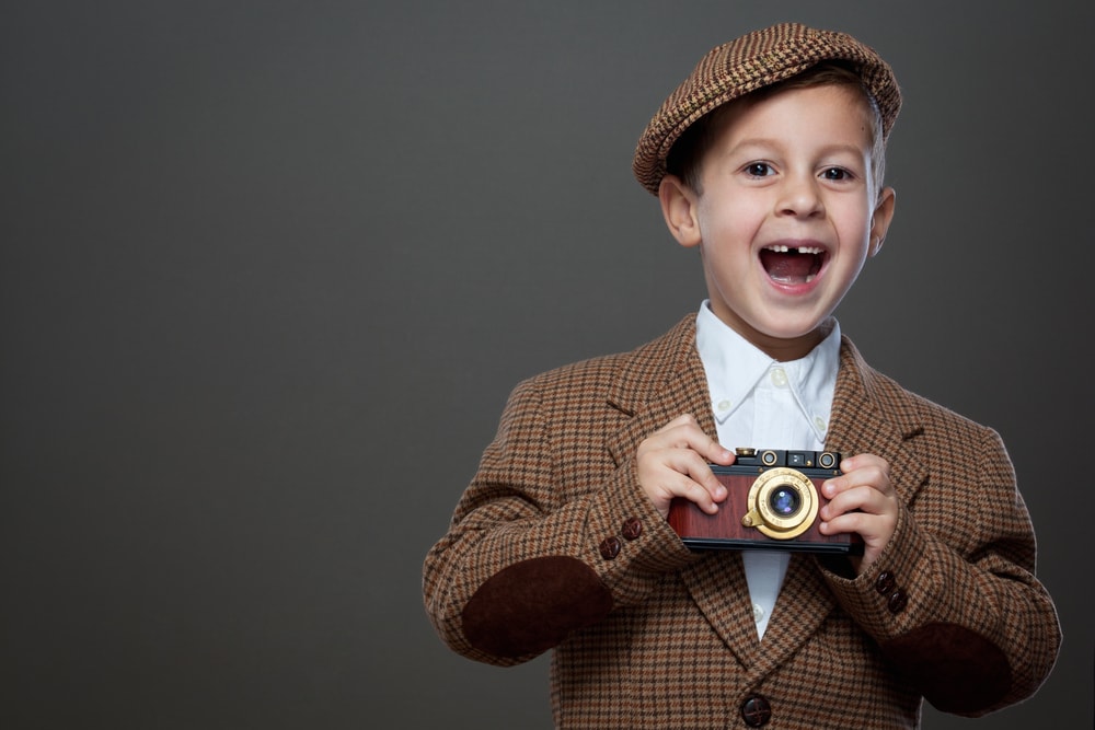shutterstock_230351719 Cute boy with vintage photo camera on the grey background. ( Retro style.)