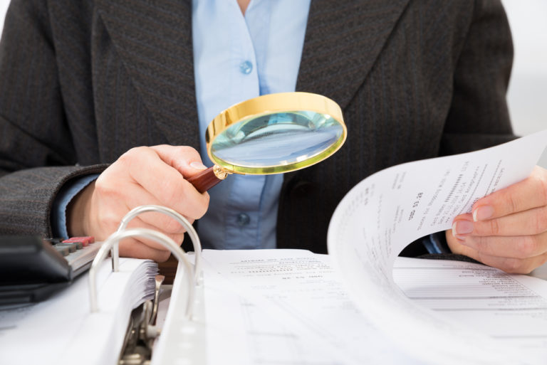 shutterstock_270438128 Close-up Of Businessperson Checking Bills With Magnifying Glass
