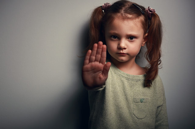 shutterstock_258302645 Angry kid girl showing hand signaling to stop useful to campaign against violence and pain on dark background. Closeup portrait