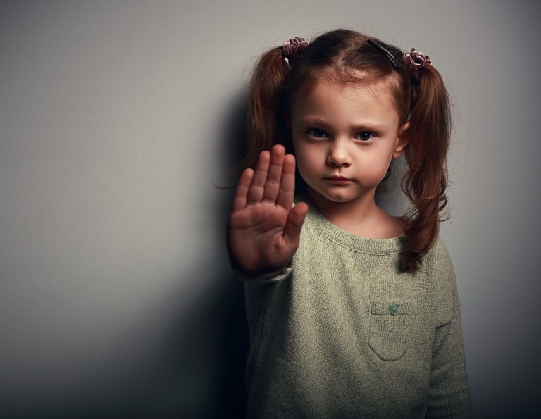 shutterstock_258302645 Angry kid girl showing hand signaling to stop useful to campaign against violence and pain on dark background. Closeup portrait
