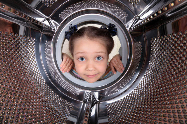 shutterstock_104976929 A curious little girl looks into the empty drum washing machine