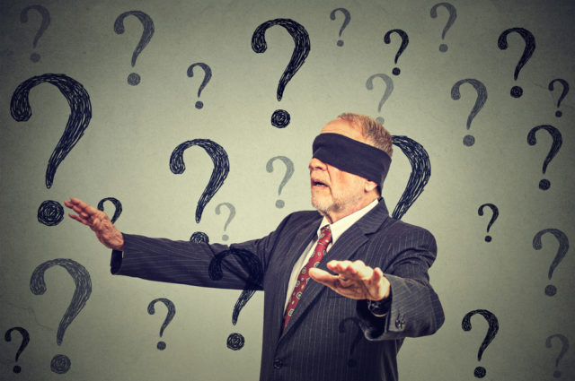 shutterstock_357493934 Portrait business man blindfolded stretching his arms out walking through many questions isolated on gray wall background