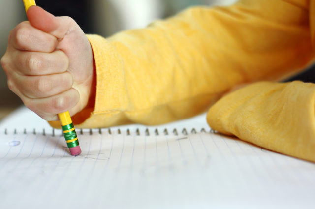 shutterstock_175759085 a child has made a mistake while writing and is holding a pencil and erasing on white notebook paper