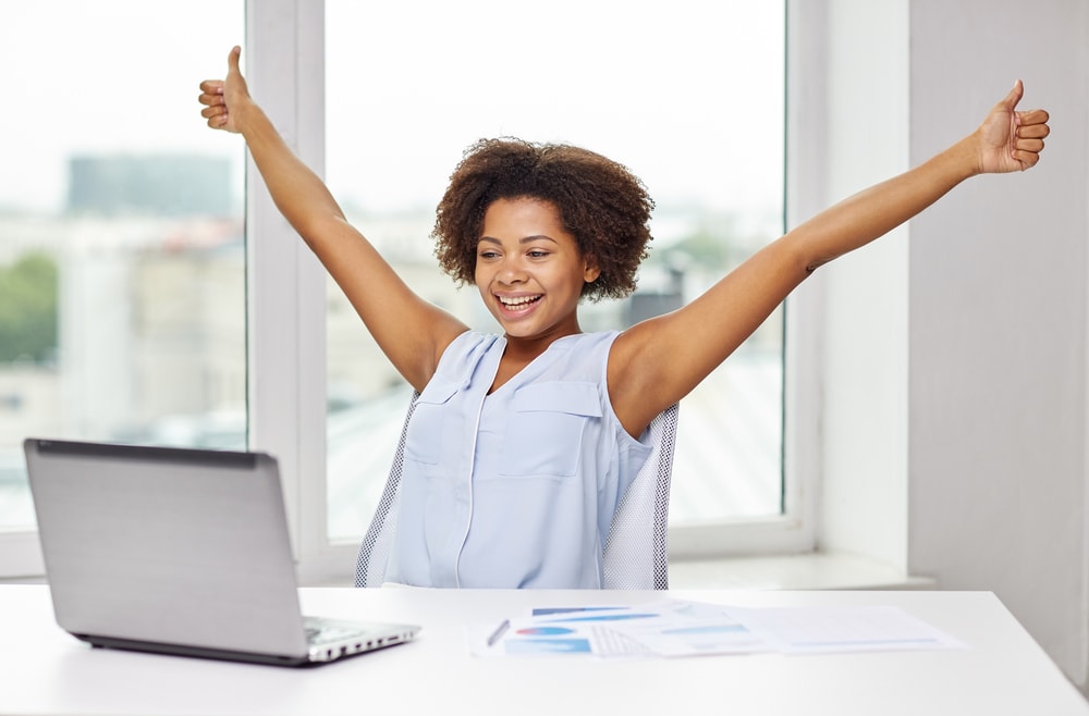 shutterstock_302657888 education, business, success, gesture and technology concept - happy african american businesswoman or student with laptop computer and papers showing thumbs up and celebrating triumph at office