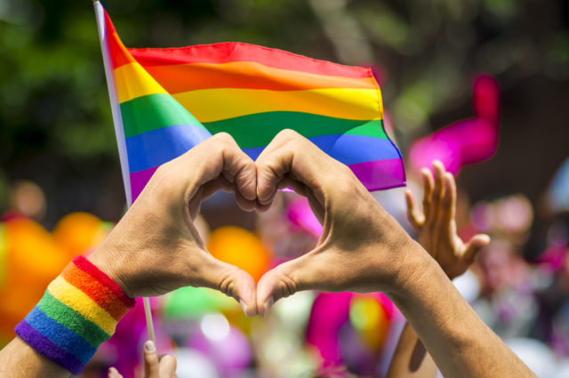 Supporting Hands Make Heart Sign And Wave In Front Of A Rainbow Flag