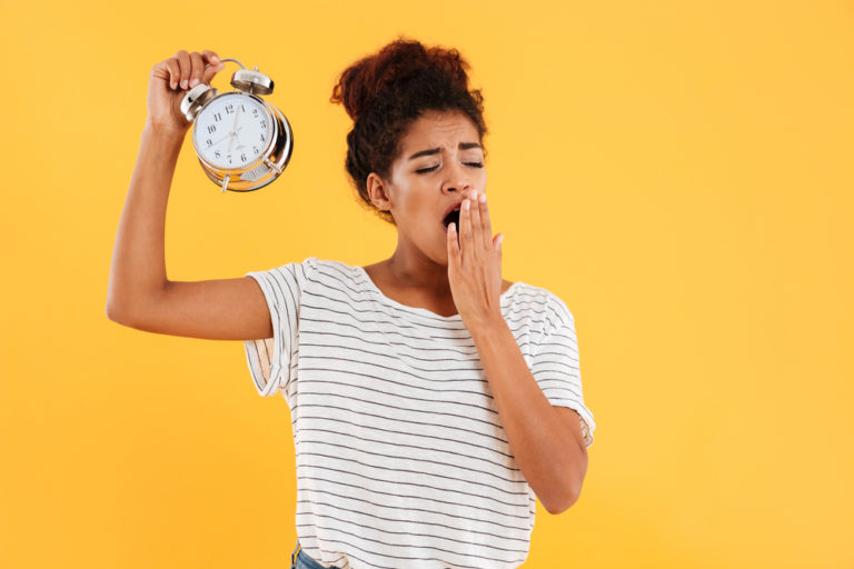 Tired,african,woman,yawns,and,holding,alarm,clock,over,yellow