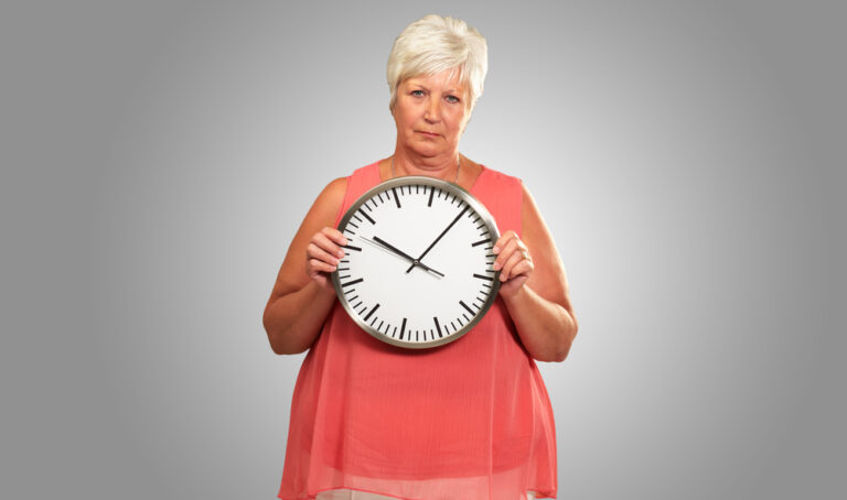 Senior,woman,holding,a,clock,on,gray,background